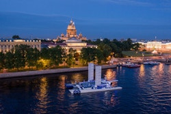 Energy Observer longe Saint-Petersbourg de nuit avec les toits des monuments illuminés en arrière plan