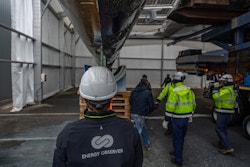 A person from behind with the Energy Observer logo looks at the boat in the hangar