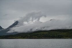 Photo de montagnes au bord de la mer avec des nuages sous un ciel gris